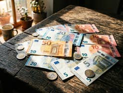 Geldnoten und Geldmünzen im Sonnenlicht auf einem Tisch.