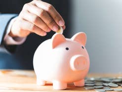 Tagesgeld: Nächste Großbank erhöht die Zinsen deutlich Hand steckt Münze in ein Sparschwein.