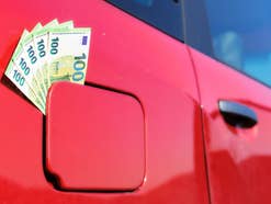 In dem Tankdeckel eines roten Autos klemmen mehrere 100-Euro-Scheine.