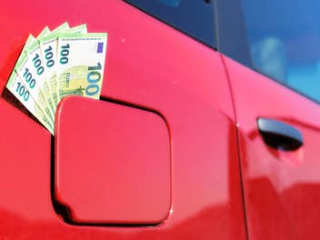 In dem Tankdeckel eines roten Autos klemmen mehrere 100-Euro-Scheine.