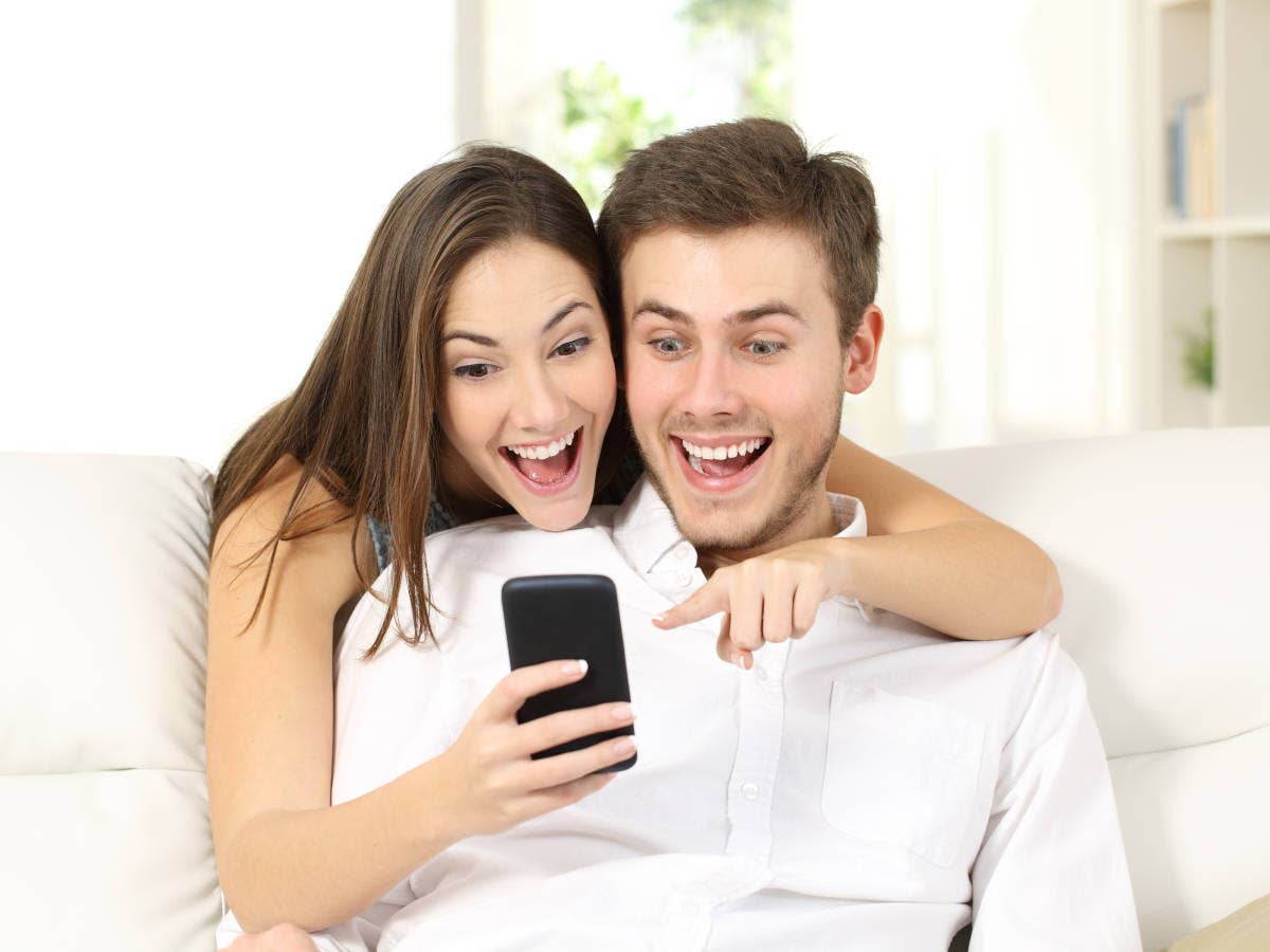 Mann und Frau sitzen auf dem Sofa und freuen sich über ein Angebot auf einem Handydisplay.