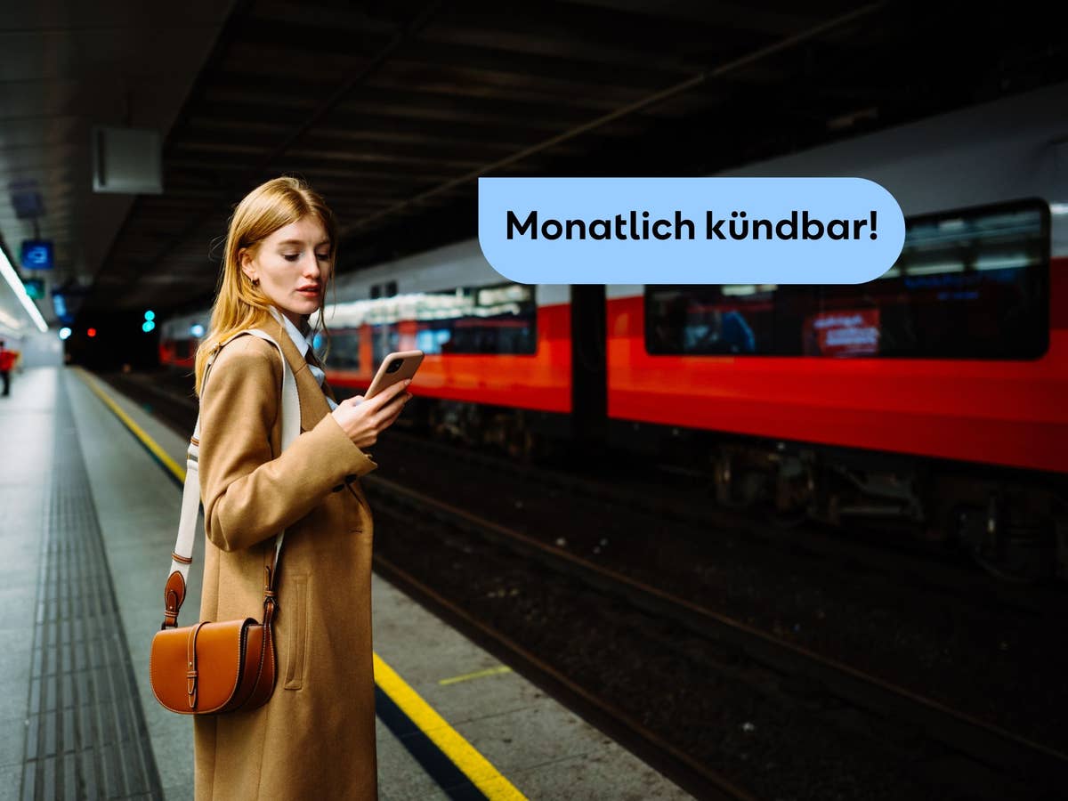 Junge Frau steht an einem Bahnhof und blickt auf ihr Handy