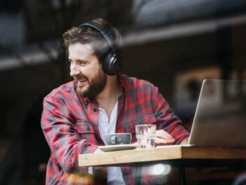 Mann sitzt mit Notebook im Café und trägt Kopfhörer von Teufel