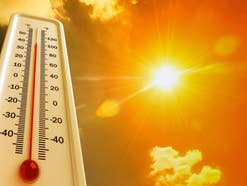 Thermometer auf der hohe Temperatur angezeigt wird, im Hintergrund eine grelle Sonne