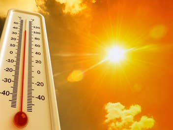 Thermometer auf der hohe Temperatur angezeigt wird, im Hintergrund eine grelle Sonne