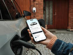 Ein E-Auto an einer Ladebuchse, zusammen mit einem Smartphone