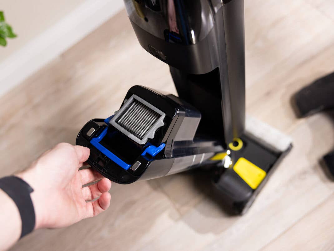 Eine Hand entnimmt den dunklen Kunststoffbehälter mit sichtbarem Lamellenfilter aus der Vorderseite des Tineco Staubsaugers.