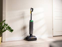Ein moderner, dunkler Akku-Nass-Trockensauger steht aufrecht an einer weißen Wand auf hellem Holzboden.
