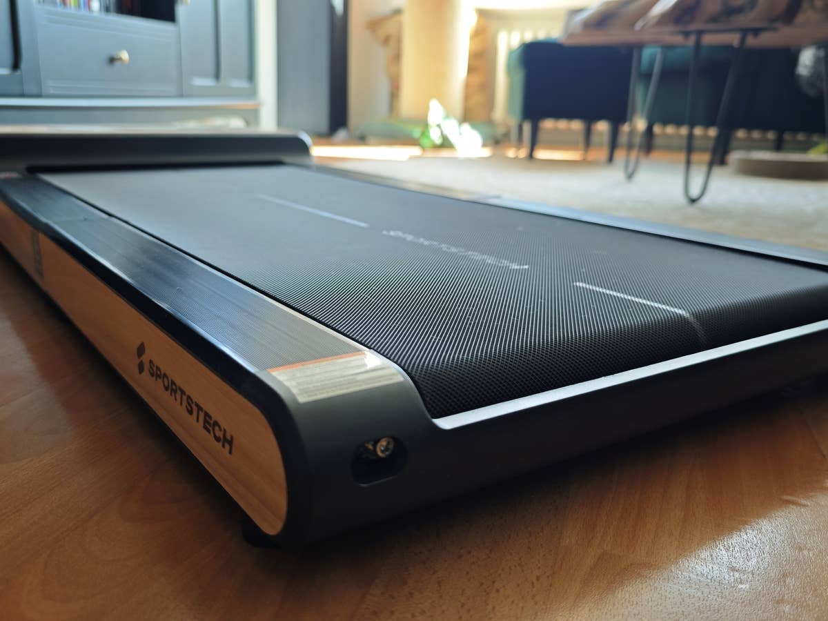 Das WoodPad Pro von Sportstech sieht nicht nur schick aus, sondern hat auch ordentlich was auf dem Kasten. Woodpad Pro liegt im Wohnzimmer auf Boden, tiefe Perspektive von unten, man sieht Möbel, einen Teppcih