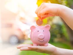 Hand steckt Geld in ein Sparschwein.