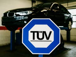 TÜV-Logo vor einem Auto auf einer Hebebühne.