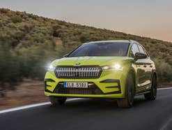 Skoda Enyaq mit eingeschalteten Frontscheinwerfern auf einer Straße.