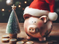 Sparschwein mit Weihnachtsmütze steht vor Euro-Geldmünzen.