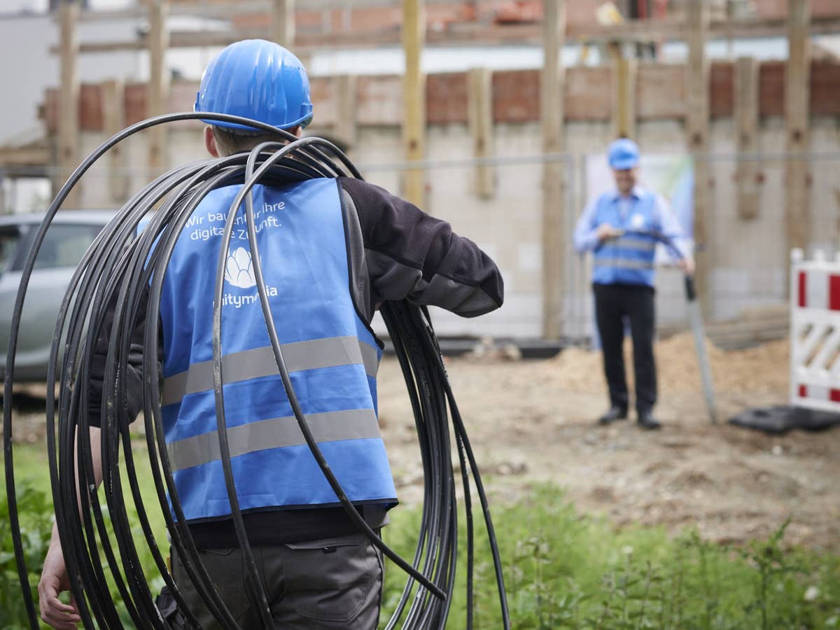 Ein Techniker mit Unitymedia-Weste trägt Glasfaser-Leerrohre zu einer Baustelle