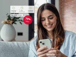 Unlimited-Kracher: Dieses Angebot ist extrem selten Eine Frau sitzt auf dem Sofa und schaut auf ihr Smartphone, Hinweise auf ein Angebot mit 70 Prozent Rabatt sind zu sehen