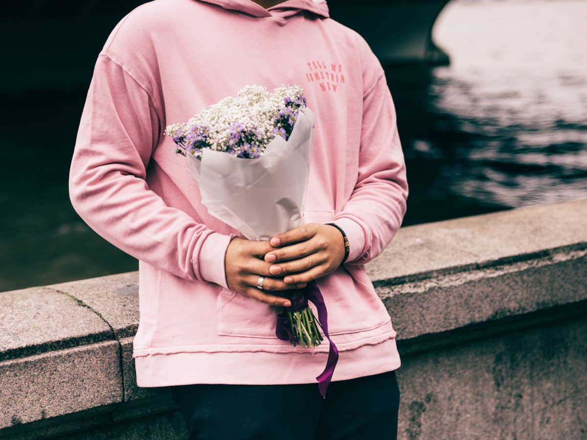 Mann steht an einer Mauer und hält einen Blumenstrauß in der Hand.