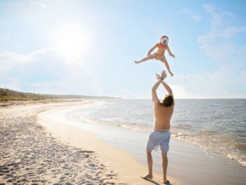 Ein Vater wirft sein Kind am Strand in die Luft