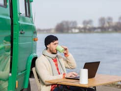 Ein Man sitzt an einem Fluß an einem Campingtisch und nutzt den Vodafone GigaVube