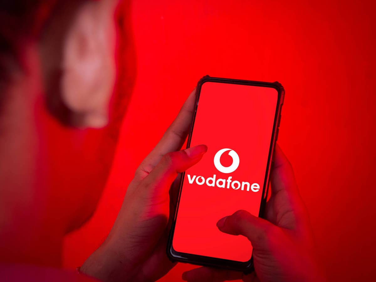 Mannschaut auf ein Handy, auf dem ein Vodafone-Logo abgebildet ist.