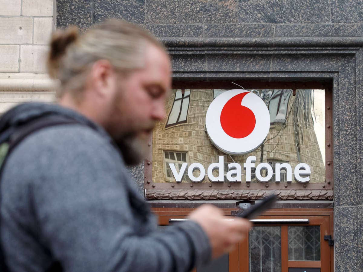 Mann mit einem Smartphone in der Hand vor einem Vodafone-Shop.