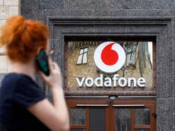 Vodafone-Logo an einer Hausfassade mit einer telefonierenden Frau im Vodergrund.