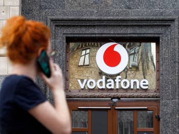 Vodafone-Logo an einer Hausfassade mit einer telefonierenden Frau im Vodergrund.