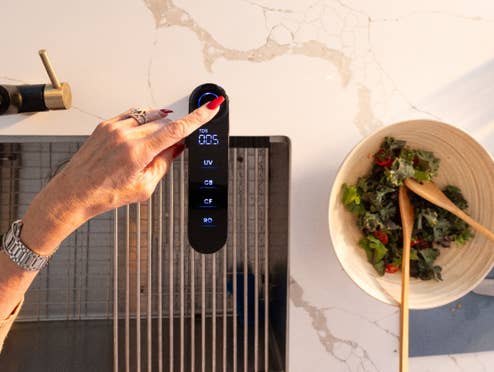 Eine Hand bedient den Waterdrop Wasserhahn. Daneben steht eine Schüssel mit Salat auf einer hellen Küchenarbeitsfläche.