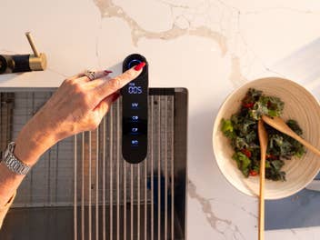 Eine Hand bedient den Waterdrop Wasserhahn. Daneben steht eine Schüssel mit Salat auf einer hellen Küchenarbeitsfläche.