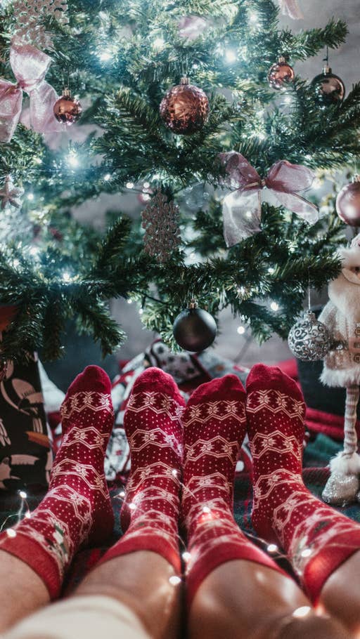 Zwei Paar Füße in Weihnachtssocken liegen vor einem geschmückten Weihnachtsbaum.