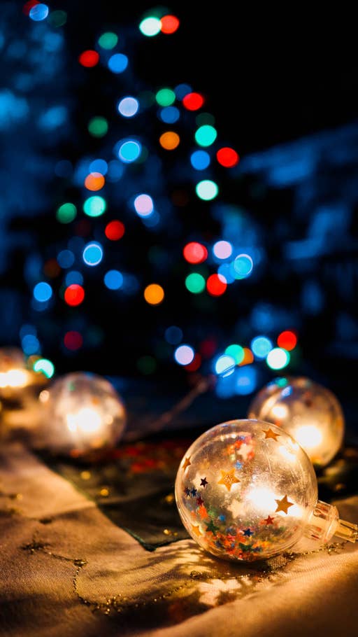 Goldene Weihnachtskugeln im Vordergrund, während im Hintergrund ein Tannenbaum bunt leuchtet.