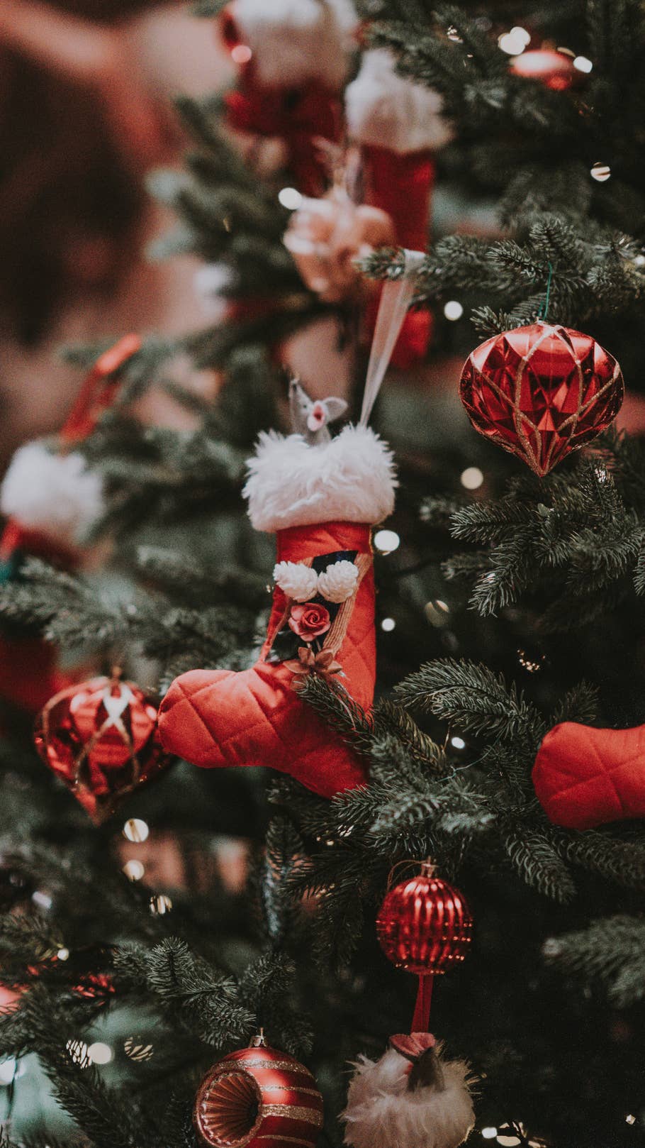 Ein roter Nikolausstiefel hängt mit anderem roten Schmuck an einem Tannenbaum.