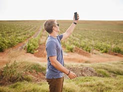 Ein Mann steht auf einem Feld und hält sein Handy in die Höhe