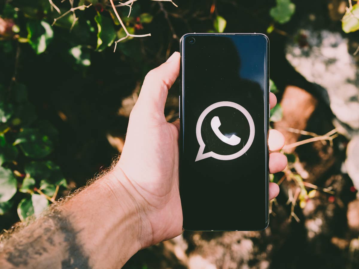 WhatsApp-Logo auf einem schwarzen Handybildschirm, das in einer Hand festgehalten wird.