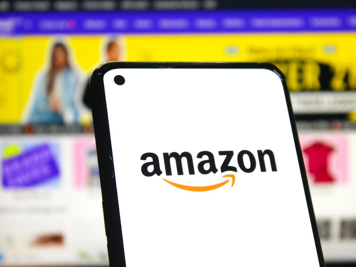 wichtige-aenderung-beim-bestellen-warum-der-amazon-einkauf-fuer-viele-kunden-ab-sofort-teurer-wird Amazon Logo auf Smartphone vor Screenshot der Amazon-Webseite