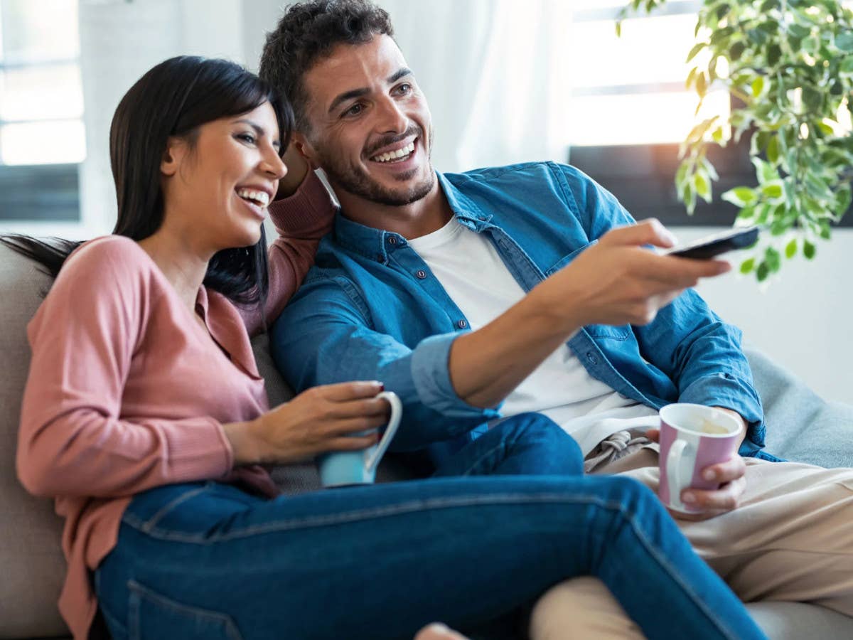 Eine Frau und ein Mann sitzen auf einem Sofa, er bedient eine TV-Fernbedienung