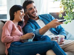 Eine Frau und ein Mann sitzen auf einem Sofa, er bedient eine TV-Fernbedienung