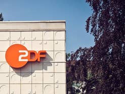 Das Logo des ZDF ist an einem Haus befestigt, rechts ist ein Baum zu sehen