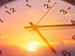 Ein Sonnenaufgang, der sich in dem Ziffernblatt einer Uhr spiegelt.