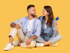 Zwei Personen schauen sich an, der Mann hält ein Smartphone, die Frau eine Kredikarte